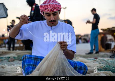 Doha, Qatar - 29 novembre 2023 : un homme arabe répare un filet de pêche pendant le festival des roulements à voile dans le village de Katara. Banque D'Images