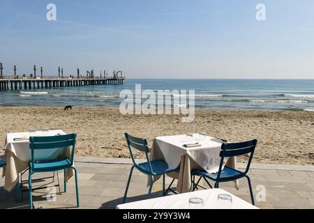 Tables posées sur le front de mer avec la plage vide et la jetée en arrière-plan un jour ensoleillé de printemps, Alassio, Savona, Ligurie, Italie Banque D'Images