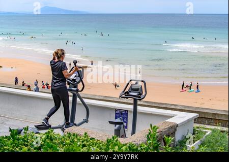 France, Pyrénées-Atlantiques (64), pays Basque, une femme sur un appareil du parcours de santé et de sport côtier avec vue sur l'océan à côté de la plage la Côte des Basques Banque D'Images