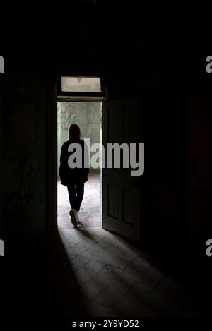 Silhouette de personne inconnue marchant dans un bâtiment abandonné vers une lumière vive Banque D'Images