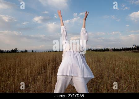 Jeune femme portant une robe blanche dansant à l'extérieur contre un ciel nuageux bleu. Banque D'Images