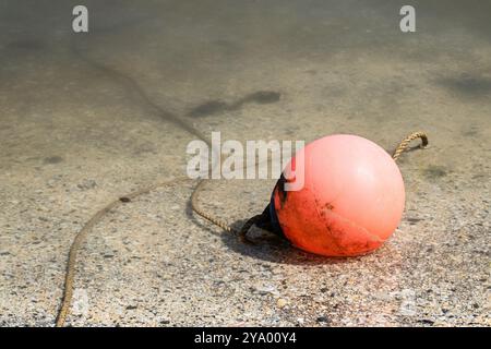 Une bouée rouge fixée par une corde reposant sur un fond marin sablonneux à marée basse en eau peu profonde Banque D'Images