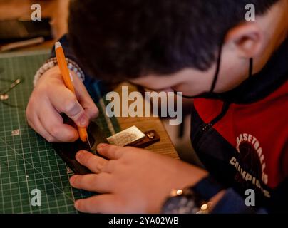 Main masculine travaillant sur le portefeuille en cuir dans son atelier. Doha, Qatar 7 février 2021 Banque D'Images