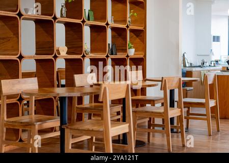 Un intérieur de café moderne avec des tables et des chaises en bois. Le fond présente une étagère en bois élégante avec des objets décoratifs et des plantes. T Banque D'Images