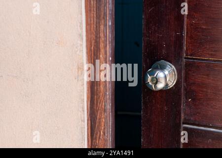 Une vue rapprochée d'une porte en bois avec une poignée de porte en métal brillant. La porte est partiellement ouverte, révélant un intérieur sombre. La texture en bois est visible, co Banque D'Images