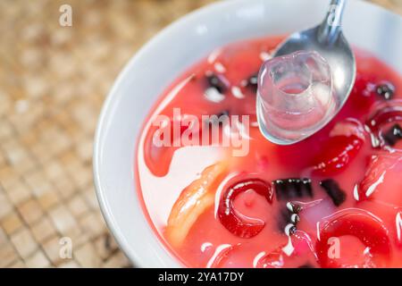 Gros plan d'un bol de dessert coloré avec gelée, morceaux de fruits et une cuillère. Le dessert a une teinte rouge vibrante avec différentes formes de gelée an Banque D'Images