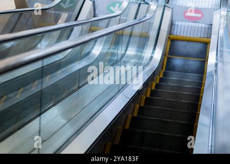 Une vue rapprochée d'un escalier roulant, mettant en valeur les marches métalliques et les garde-corps en verre. L'escalier roulant descend, avec des marques de sécurité jaunes visibles. S Banque D'Images