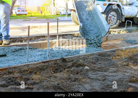 Camion malaxeur de béton coulant du béton frais sur des barres renforcées pour la construction d'un nouveau trottoir Banque D'Images