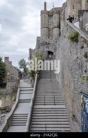 Des marches de pierre mènent vers le haut le long d'un mur historique du château, sous un ciel nuageux, le Mont-Saint-Michel Banque D'Images