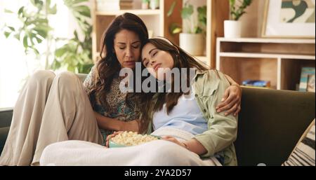Film, mère mature et fille triste sur le canapé avec collage, pop-corn et regarder la télévision dans le salon. Week-end, câlin et maman sur le canapé avec fille pour Banque D'Images