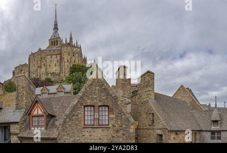 Bâtiments historiques avec une impressionnante église en arrière-plan, sous un ciel nuageux, le Mont-Saint-Michel Banque D'Images