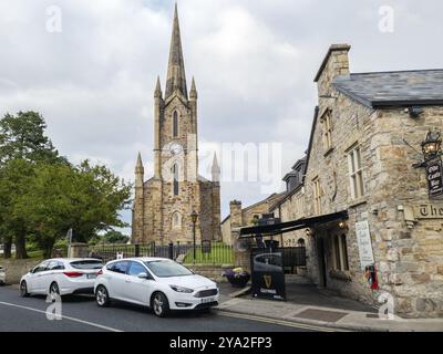 Grande église gothique avec haute tour à côté d'une route de campagne et de voitures garées, Donegal Banque D'Images