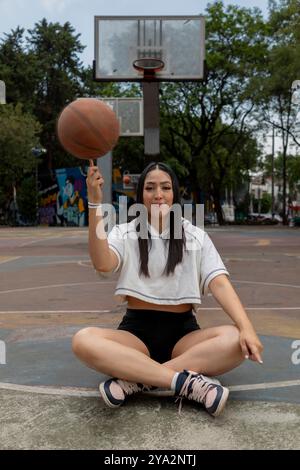 Portrait d'une joueuse de basket-ball assise sur le sol faisant tourner la balle sur son doigt Banque D'Images