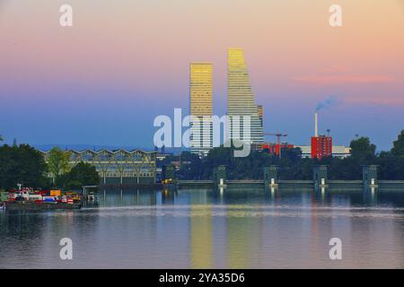 Deux gratte-ciel se reflètent dans l'eau au coucher du soleil. Les environs montrent des espaces verts et des éléments industriels, Roche Towers, Hoffmann- la Roche, tal Banque D'Images