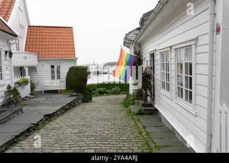 Une rue sereine dans le quartier historique de Gamle Stavanger, avec une maison en bois blanc avec un drapeau arc-en-ciel LGBT accroché à sa façade et à la mer Banque D'Images