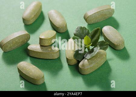 Pilules fines herbes et vitamine Green posées librement sur fond vert Banque D'Images