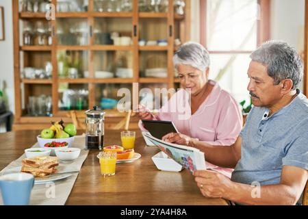 Journal, manger le petit déjeuner et couple senior avec tablette pour lire les nouvelles du matin, histoire et mise à jour. Nourriture, homme et femme avec la technologie dedans Banque D'Images