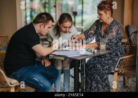 Femme âgée aidant le jeune homme avec le syndrome de Down et la fille dessiner ensemble Banque D'Images