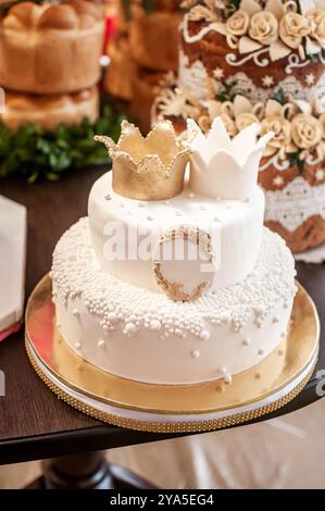 Elégant gâteau à deux niveaux orné de couronnes dorées et de perles. Banque D'Images