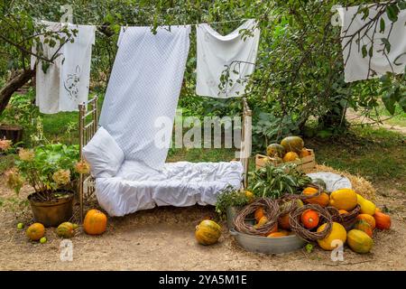 Citrouilles sur le sol. Lit en fer et linge de lit. Draps blancs accrochés à une corde dans le jardin. Installation d'automne dans le jardin. Banque D'Images