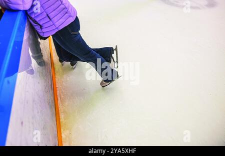 Patineur sur glace appuyé contre la barrière de la patinoire tout en se tenant debout sur des patins, portant une veste violette et un Jean à une patinoire intérieure. Suède. Banque D'Images