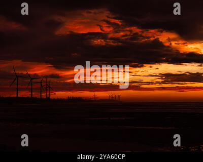 Des nuages ardents remplissent le ciel de teintes orange et rouge vives tandis que les éoliennes se dressent au loin, créant une scène de coucher de soleil spectaculaire et captivante Banque D'Images