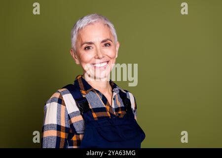 Portrait photo de joli sourire professionnel professionnel senior femme bricoleur porter des vêtements de travail bleus dans l'ensemble isolé sur fond de couleur kaki Banque D'Images