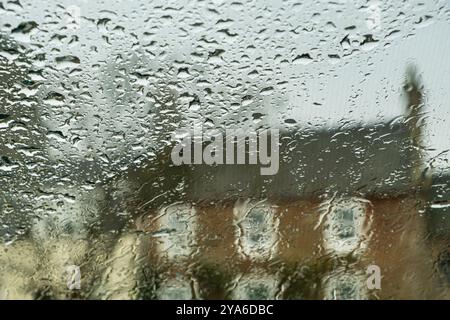 Pluie tombant sur le pare-brise d'une voiture provoquant de mauvaises conditions de conduite, visibilité déformant l'arrière-plan Banque D'Images