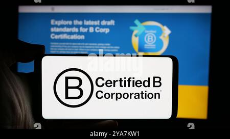 Personne tenant un téléphone portable avec le logo de l'organisme de certification B Corporation (B Corp) sur l'écran devant la page Web. Concentrez-vous sur l'affichage du téléphone. Banque D'Images