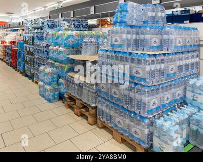 Italie - 12 octobre 2024 : eau dans des bouteilles en plastique de différentes marques dans des emballages empilés sur des palettes exposées dans l'allée des supermarchés italiens Banque D'Images