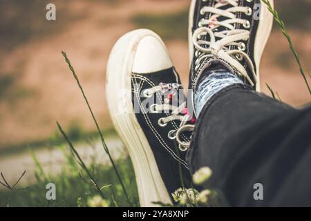 Une jeune fille en baskets noires et blanches se relaxant assise sur une pelouse verte en été. Reposez-vous dans la nature. Herbe verte dans un jardin, parc. Chaussure pour filles. Banque D'Images