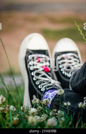 Une jeune fille en baskets noires et blanches se relaxant assise sur une pelouse verte en été. Reposez-vous dans la nature. Herbe verte dans un jardin, parc. Chaussure pour filles. Banque D'Images