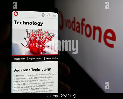 Dans cette illustration photo, une personne tient un téléphone portable avec la page Web de la société de télécommunications britannique Vodafone Group plc devant le logo. Banque D'Images