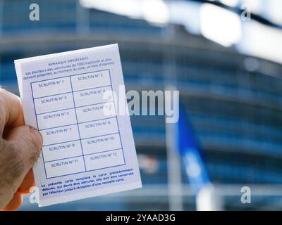 Strasbourg, France - 7 juin 2024 : gros plan du dos d'une carte électorale française, montrant des espaces pour enregistrer les sessions de vote, avec le bâtiment du Parlement défocalisé en arrière-plan Banque D'Images