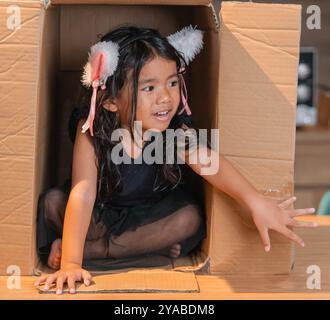 Une petite fille ludique habillée dans une boîte en carton avec des oreilles de chat adorables sur sa tête Banque D'Images