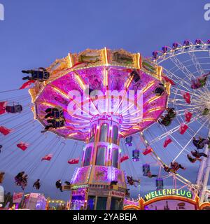 Une foire animée au crépuscule, illuminée par une grande roue et un carrousel à chaînes coloré, Cannstadter Volksfest, Stuttgart-Bad Cannstadt, Baden-Wï¿½ Banque D'Images