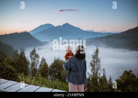 Mère et enfant appréciant un lever de soleil serein de montagne avec paysage brumeux Banque D'Images