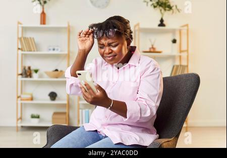 Femme afro-américaine d'âge moyen regardant un smartphone avec des lunettes vers le haut, gros plan Banque D'Images