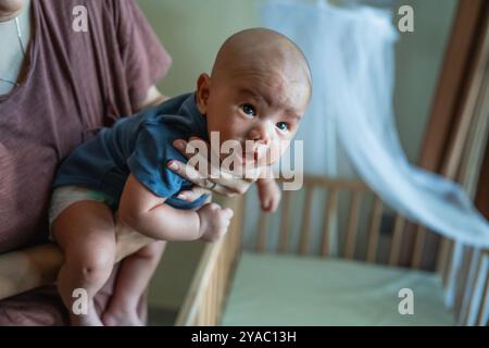 Un bébé curieux dans un berceau, embrassé par un parent doux et aimant Banque D'Images