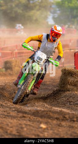 Pilote de motocross en action tournant et pliant sa moto dans un virage serré sur un terrain poussiéreux, expulsant la poussière de sa roue arrière lors d'un e extérieur Banque D'Images