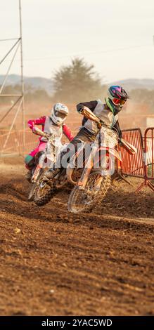 Pilote de motocross effectuant un virage serré sur une piste de terre humide échappant à un adversaire qui suit de près lors d'une compétition de course de moto d'endurance. Banque D'Images