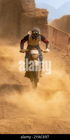 Pilote de motocross dans l'action course sur une pente raide entourée d'un terrain poussiéreux dans une course d'endurance. Banque D'Images