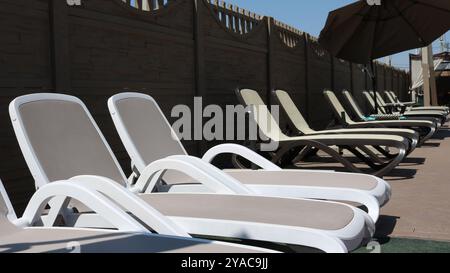 Chaises longues blanches et beiges, parasol et clôture en briques brunes, coin salon au bord de la piscine Banque D'Images