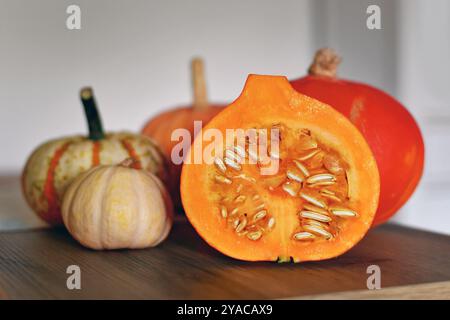 Citrouille Hokkaido coupée en deux montrant des graines sur une planche à découper avec d'autres citrouilles en arrière-plan Banque D'Images