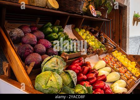 Une exposition colorée de légumes et de fruits, y compris des tomates, des poivrons et des courges. Les produits sont disposés dans des caisses et des paniers en bois, créant un Banque D'Images