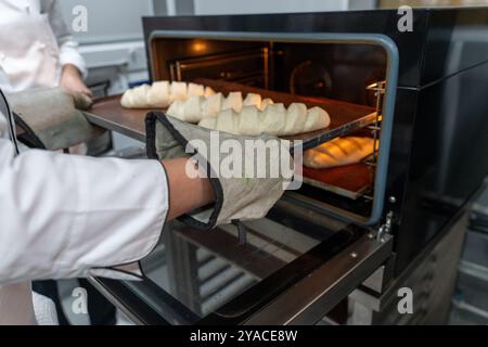 Le boulanger met les miches de pain au four. Faire du pain dans une mini boulangerie. Photo de haute qualité Banque D'Images