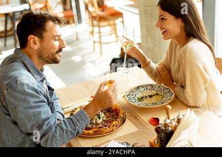 Deux personnes savourent leurs boissons à une table en bois, immergées dans une ambiance de restaurant détendue, tout en étant profondément dans la conversation et les rires. Banque D'Images