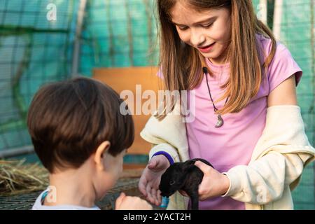 Fille caucasienne enfant avec petit frère tenant un bébé lapin noir dans ses mains. Banque D'Images