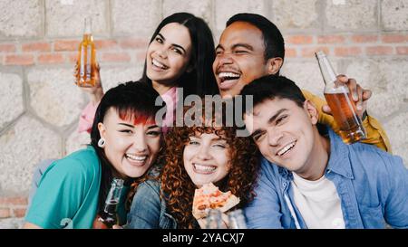 Amis divers mangeant de la pizza et buvant de la bière à l'extérieur. Jeunes heureux célébrant avec de la nourriture à emporter Banque D'Images