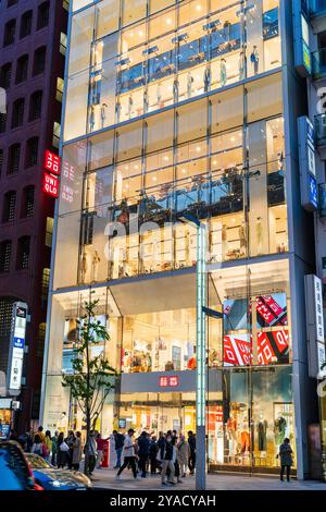 Soirée de l'autre côté de la rue vue de l'entrée du magasin phare Uni Qlo à la mode sur le Ginza. Mannequins habillés dans les vitrines. Banque D'Images